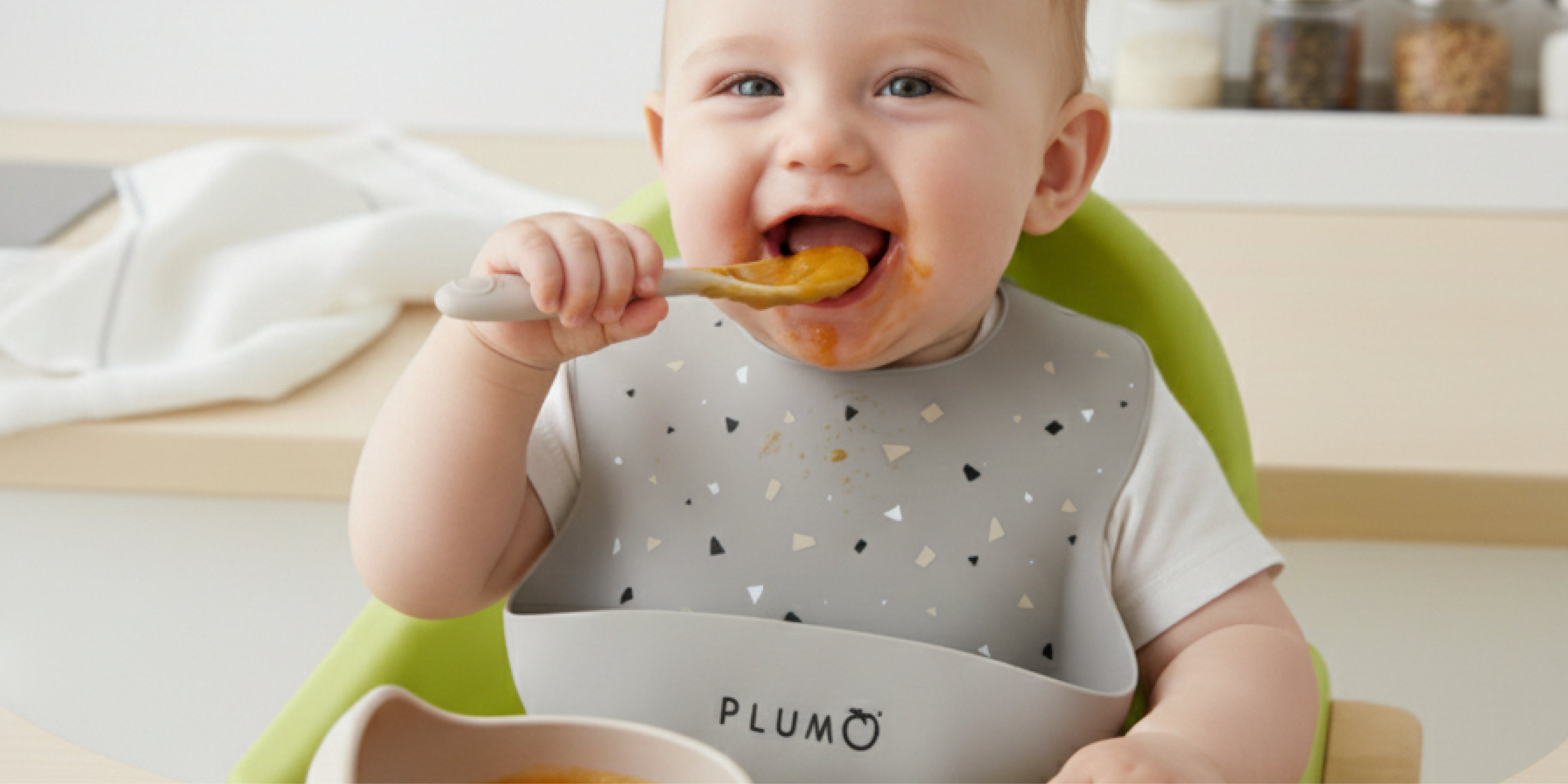 cute baby in a hi chair with plum brand feeding smock bowl and cup