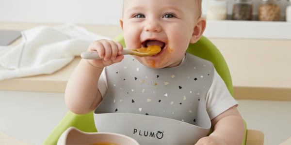 cute baby in a hi chair with plum brand feeding smock bowl and cup