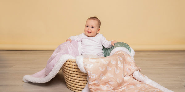 cute baby sitting in a basket of fleece blankets with nordic prints